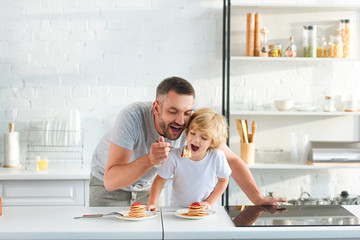 happy father and son eating pancakes at kitchen