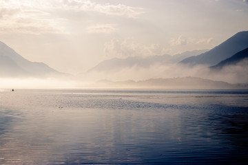 Early morning sunrise on lake Como in Italy. The sun is breaking through as the fog starts to disappear from the surface of the water. After that it is time to wait for the wind to go windsurfing