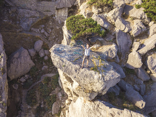 aerial shot happy teenager with raised hands standing on the mountain edge during sunrise summer season
