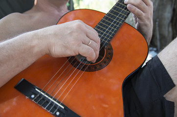A man on vacation playing the guitar in the company of his friends on summer day; Close-up of a man's fingers on a guitar strings