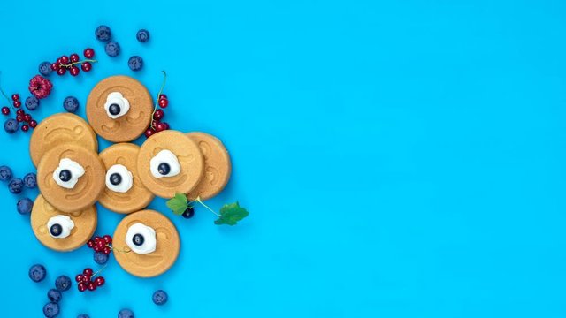 Stop motion food background. Delicious mini smile pancakes with berries  on blue surface, top view, dynamic scene, 4k video