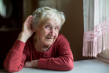 A hard-of-hearing elderly woman holds her hand near her ear.