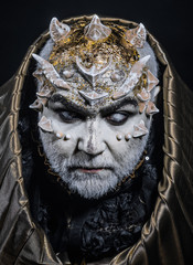 Man with thorns or warts, face covered with glitters. Demon with golden hood on black background....