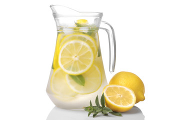 Homemade lemonade with mint and ice in a glass jug and a glass next to fresh lemon on a white...