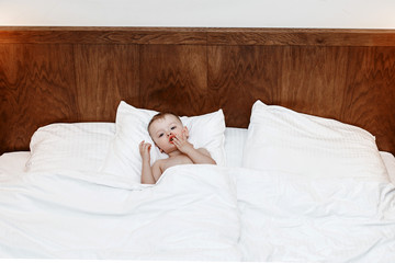 The child is in bed. Boy on a big bed between a blanket and a pillow. A little baby is sitting in bed and eating.