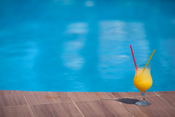 glass of yellow juice with ice against the background of the pool in summer