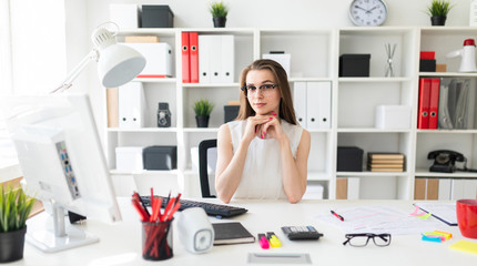 Beautiful young girl is sitting at the table in the office.