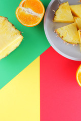 Pieces of pineapple and oranges on a white plate, chopped pineapple and half orange on a colorful background, tropical fruit salad in pop art style, vegetarian food