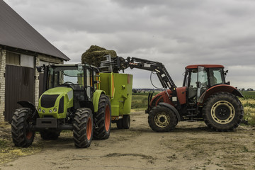 Agricultural machinery and equipment.The tractor with the loader loads a bale of silage in the distributor of mixed fodders for cows.Podlasie, Poland.