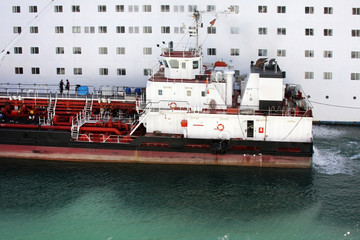 Delivering ship refueling big white passenger cruise liner. Refueling of heavy commercial ship in...