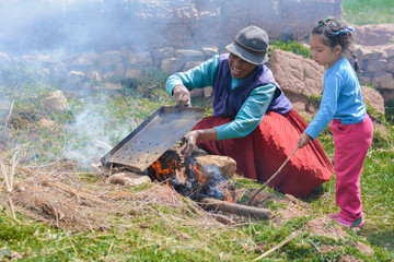 Native american grandmother with her little granddaughter preparing food in the countryside.