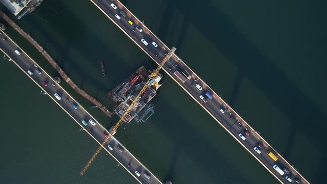 Cars ride on two bridges over the river. The camera is directed downwards rises to a greater height and rotates. Shadows of bridges in the waters of the river. Shooting with a drone.