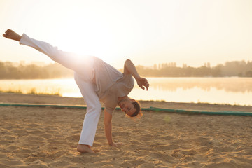 Athletic capoeira performer workout training on the beach sunris