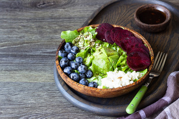 Fresh healthy salad lettuce with avocado, blueberry, beetroot and mozzarella in a brown wooden bowl.