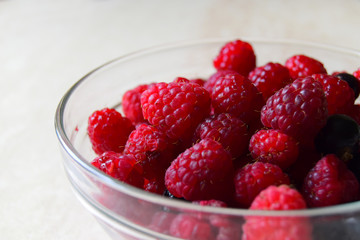Berries of raspberry and several berries of bilberry are in a glass bowl. Close up, white background