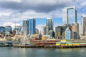 Seattle waterfront, piers 56 and 57, and skyline on a bright and cloudy day, view from the Puget Sound, Washington State, USA.