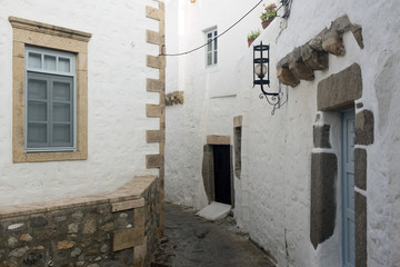 A view of a narrow street with arch and wooden windows and doors with white wall stone architecture of the island Patmos, Greece