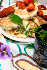 Freshly baked cottage cheese pancakes with raisins, strawberry with cup of melissa tea. Frying process. Top view