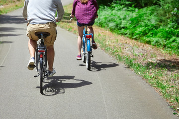 Loving married couple riding on bicycles. A man in beige shorts and a woman in a purple shirt. View from the back. Bike ride in the nature on a sunny summer day