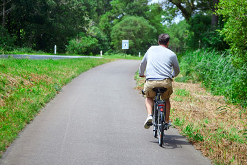 Adult man riding a bicycle. Cyclist in beige shorts. View from the back. Bike ride in the nature on a sunny summer day