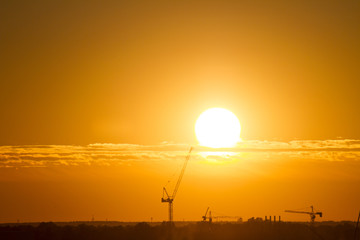 Obraz premium Sunset over the city. Tower crane. Industrial landscape. Bright sunset over the horizon