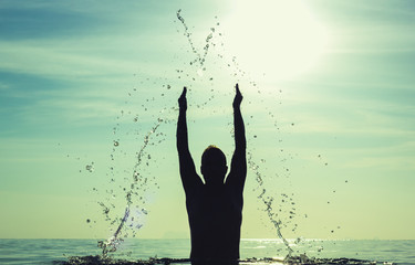 Silhouette of man with hands up splashing water forming a triangle shape at gorgeous sunset on the...