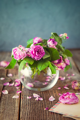 Vintage concept - bouquet of wilting tea roses in glass vase, old letters in craft paper envelopes, blank greeting card on the old wooden rustic background. Retro toned. Selective focus. copy space.