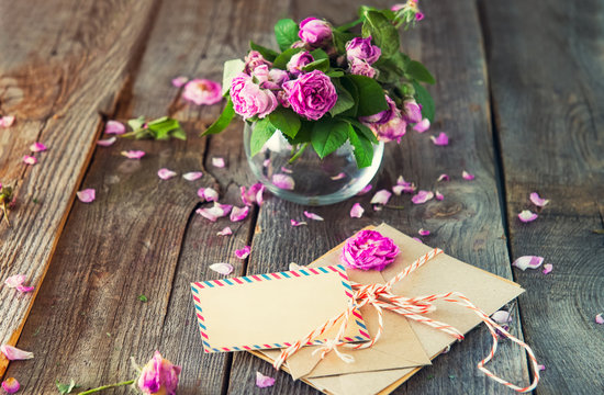 Vintage concept - bouquet of wilting tea roses in vase, pile of old letters in envelopes and blank greeting card on the old wooden rustic background. Retro toned. Selective focus. copy space.