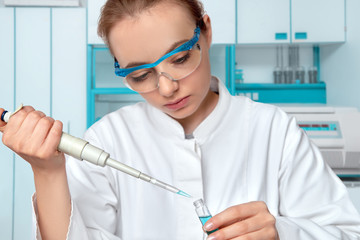 Female European researcher in protetcive glasses is loading liquid sample with automatic pipette