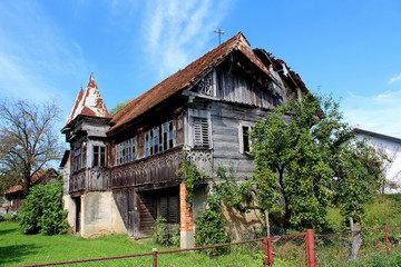 Very old partially broken down wooden house covered in green plants and abandoned many years ago on a warm sunny day