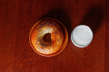 A glass of fresh milk and a delicious bagel with poppy on a wooden table. Healthy food.