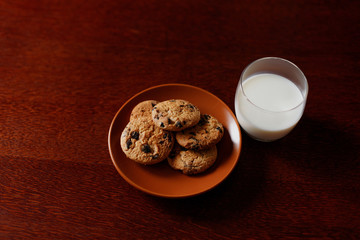 A glass of fresh milk and oatmeal cookies on a wooden table.