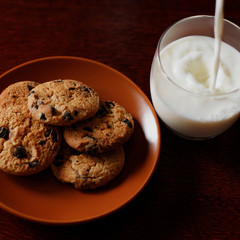 Milk is poured into a glass. Oatmeal cookies on a plate.