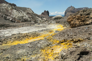 Obraz premium The outlet stream from the crater lake of the active volcano of White Island, Whakaari, off the Bay of Plenty coast, New Zealand. Yellow crystals of sulphur in the foreground.