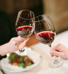Man and woman drinking red wine. In the picture, close-up hands with glasses.