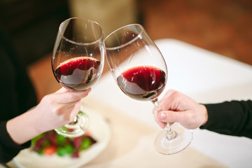Man and woman drinking red wine. In the picture, close-up hands with glasses.