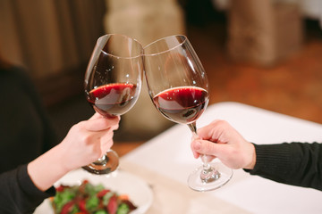 Man and woman drinking red wine. In the picture, close-up hands with glasses.