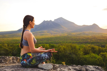 Naklejka na ściany i meble Young woman practicing yoga or pilates at sunset or sunrise in beautiful mountain location.