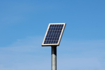 Small solar panel mounted high on top of thick grey metal pole on warm sunny winter day with clear...