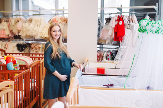Pregnant girl chooses a baby cot in the store.