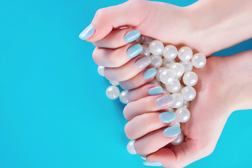 Blue nails manicure on young girl and white pearls in hands. Femininity fashion and beauty concept. Close up, selective focus
