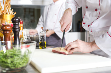 Chef cutting meat on chopping board, professional cook holding knife and cutting meat in restaurant