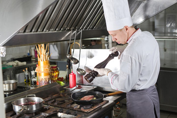 Chef in restaurant kitchen at stove with pan, cooking