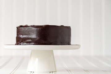 Side view of chocolate cake on a white cake platter against a white background
