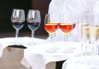 The waiters greet guests with alcoholic drinks. Champagne, red wine, white wine on trays.