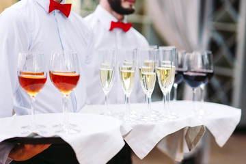 The waiters greet guests with alcoholic drinks. Champagne, red wine, white wine on trays.