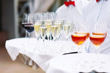 The waiters greet guests with alcoholic drinks. Champagne, red wine, white wine on trays.