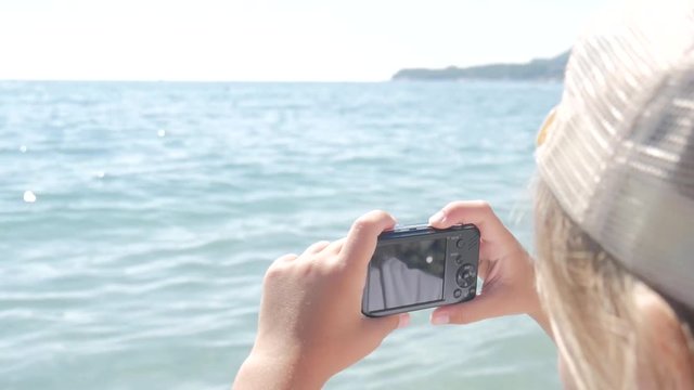 Little girl makes a photo of a beautiful view sea on a camera, close-up.