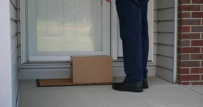A delivery man places a cardboard box on a home's front porch then rings the doorbell before leaving.  	Can be used for a contactless delivery concept.