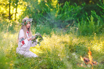 Midsummer. Woman weaving a wreath near the fire.